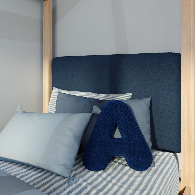 Navy blue letter "A" accent pillow on striped blue-and-white bedding with pale blue pillows and a dark upholstered headboard in a light wood canopy twin bed — modern coastal kids' bedroom decor