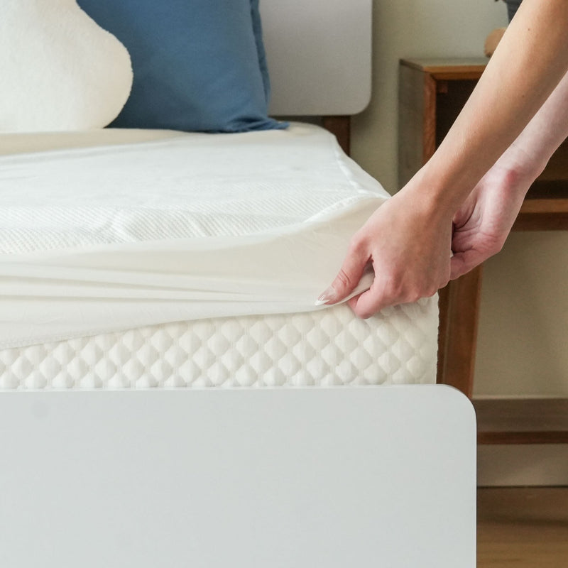 Person adjusting a white fitted sheet on a comfortable memory foam mattress.