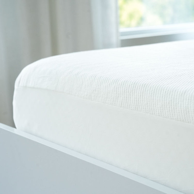 Luxury white mattress topper on modern bed frame in bright bedroom setting.
