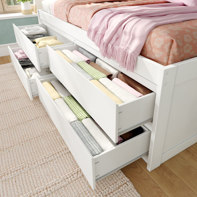 Under-bed storage drawers in white bed frame with neatly folded clothes, rolled linens, pink throw and floral bedding — space-saving bedroom organization