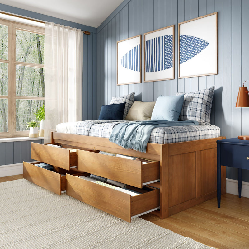 Wooden storage platform bed with multiple open pull-out drawers in a coastal blue paneled bedroom, plaid pillows, light blue throw, framed art and sunlit window