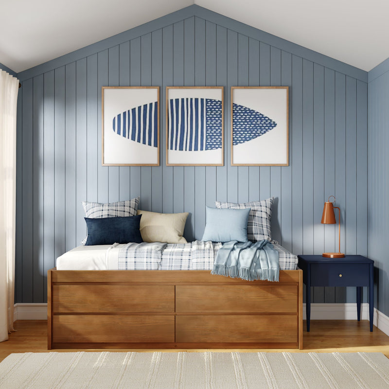 Coastal bedroom with blue shiplap accent wall, wooden storage bed, plaid and navy pillows, triptych blue abstract art and orange lamp