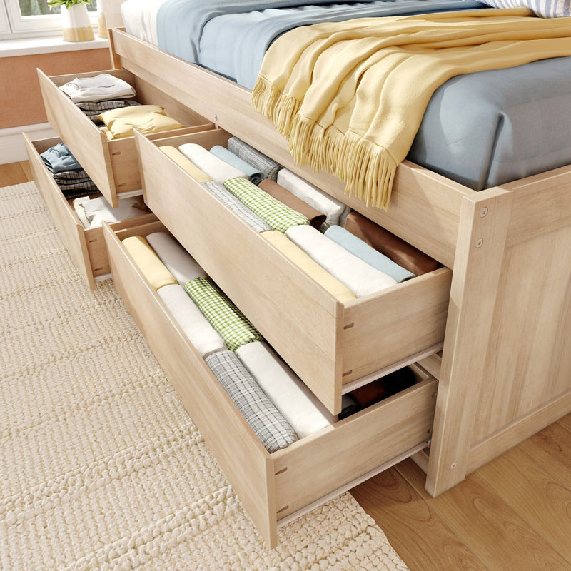Light wood storage bed with multiple under-bed pull-out drawers neatly organized with folded linens and blankets, space-saving bedroom storage solution.
