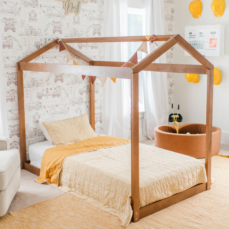 Kids bedroom with wooden house-frame bed, yellow-orange quilt, construction vehicle wallpaper and toy hard hats
