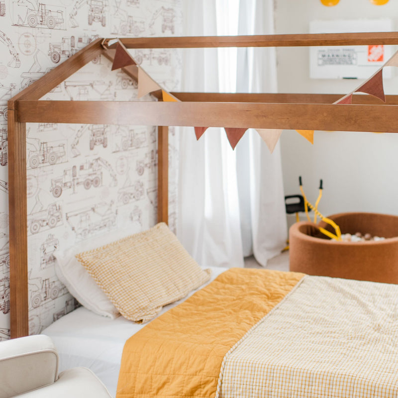 Kids bedroom nursery with wooden house-frame bed, yellow gingham bedding and quilt, construction vehicle wallpaper, triangle bunting flags and round toy storage