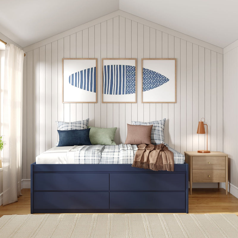 Coastal modern farmhouse bedroom with navy storage bed, plaid and solid pillows, vertical white shiplap wall, vaulted ceiling, three framed blue abstract prints, wooden nightstand and orange bedside lamp.