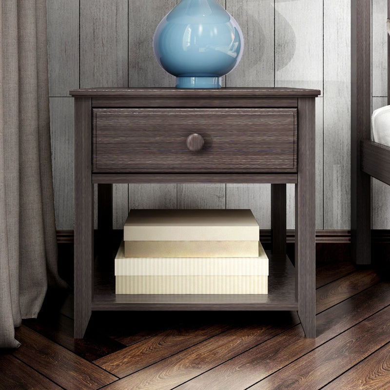 Modern dark wood nightstand with single drawer and open lower shelf holding beige storage boxes, topped with a blue ceramic lamp on hardwood bedroom floor and neutral curtain backdrop