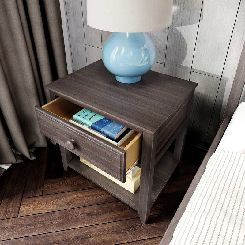 Dark wood nightstand with open drawer holding books, blue ceramic lamp with white shade on top, bedside decor on hardwood floor