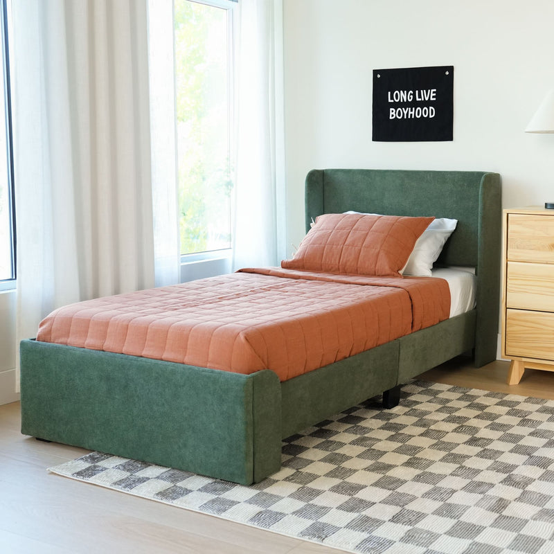 Modern boy's bedroom with green upholstered single bed, terracotta quilt and pillow, wooden nightstand, sheer curtains and "Long Live Boyhood" wall hanging