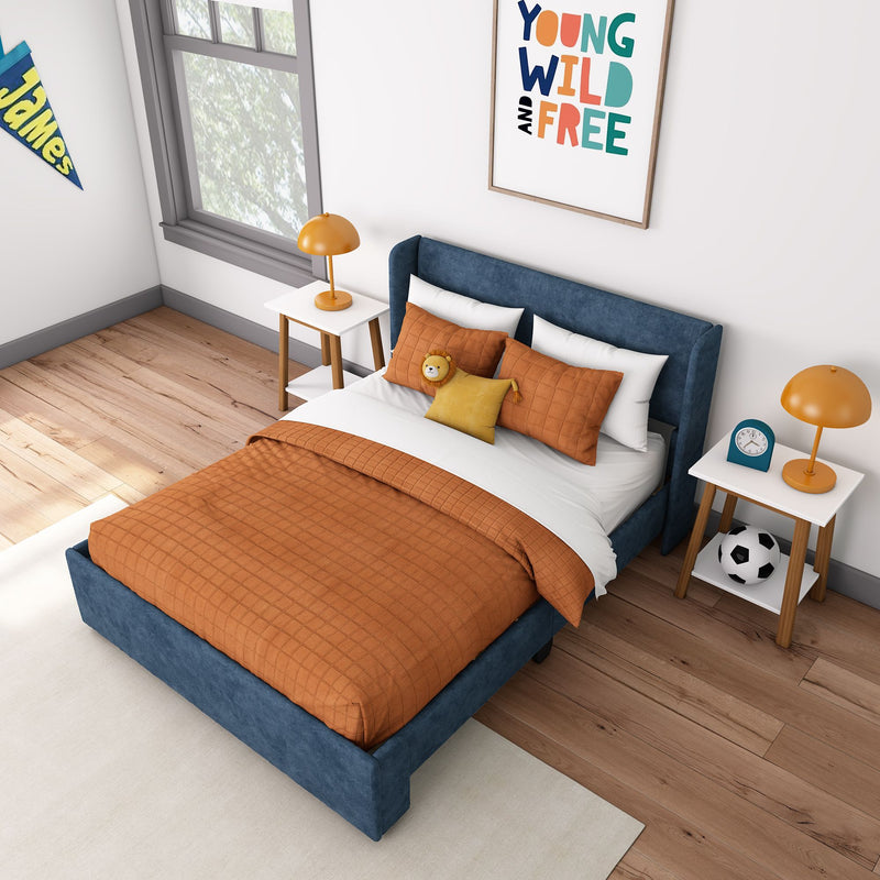 Kids bedroom with blue upholstered bed, orange quilted bedding, plush lion toy, orange bedside lamp, soccer ball and "Young Wild and Free" wall art