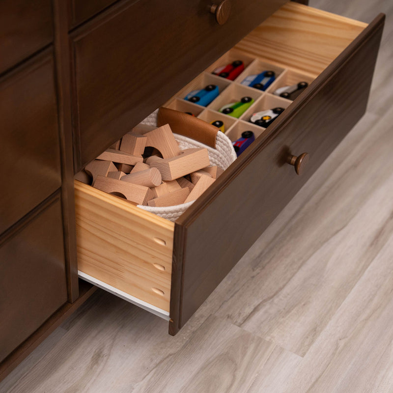 Open wooden dresser drawer with compartment organizer holding colorful wooden toy cars and natural wooden blocks in a child's bedroom