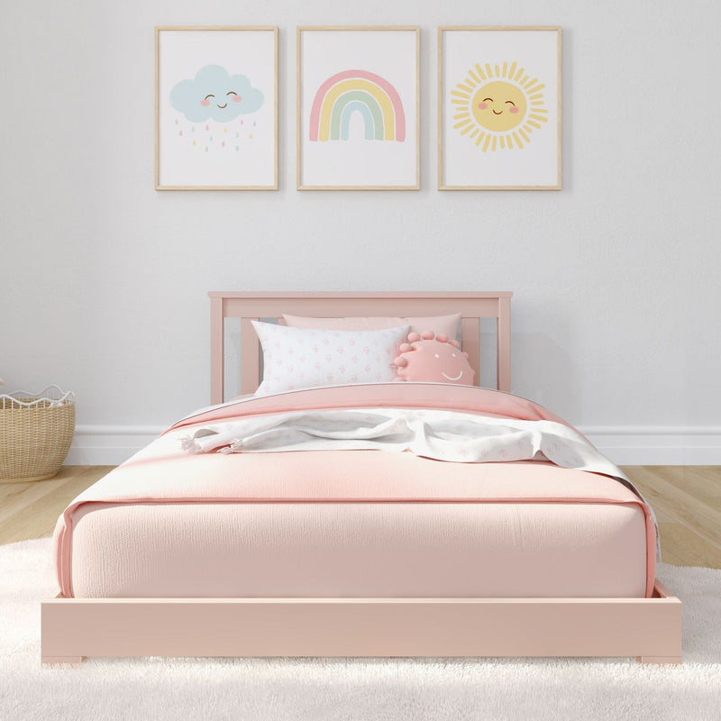 Pastel pink toddler bed with blush bedding and smiling cloud, rainbow, and sun nursery wall art in wooden frames — modern kids bedroom decor