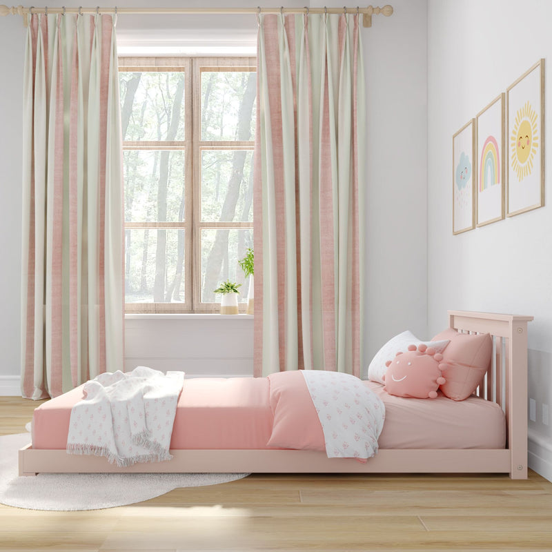 Pastel pink toddler bed with smiley sun pillow and patterned blanket, pink-and-cream striped curtains framing a wooden window in a bright nursery