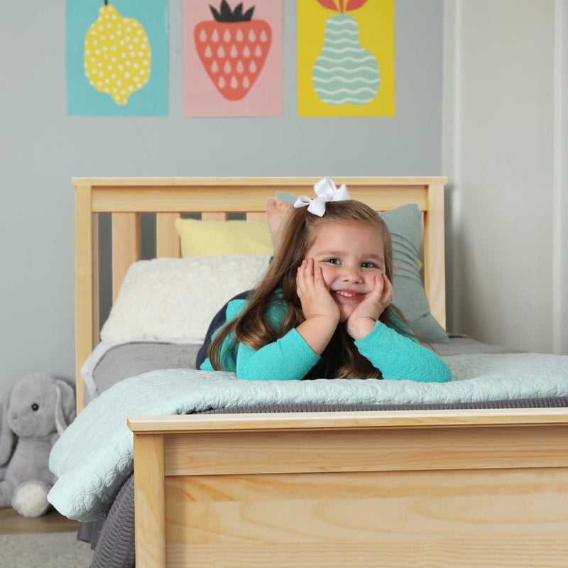Smiling child lying on a wooden bed in a pastel kids' bedroom with mint bedding, colorful fruit wall art and a plush elephant toy