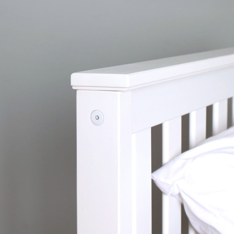 Close-up of white wooden crib headboard with slatted rails and top rail detail in a modern nursery
