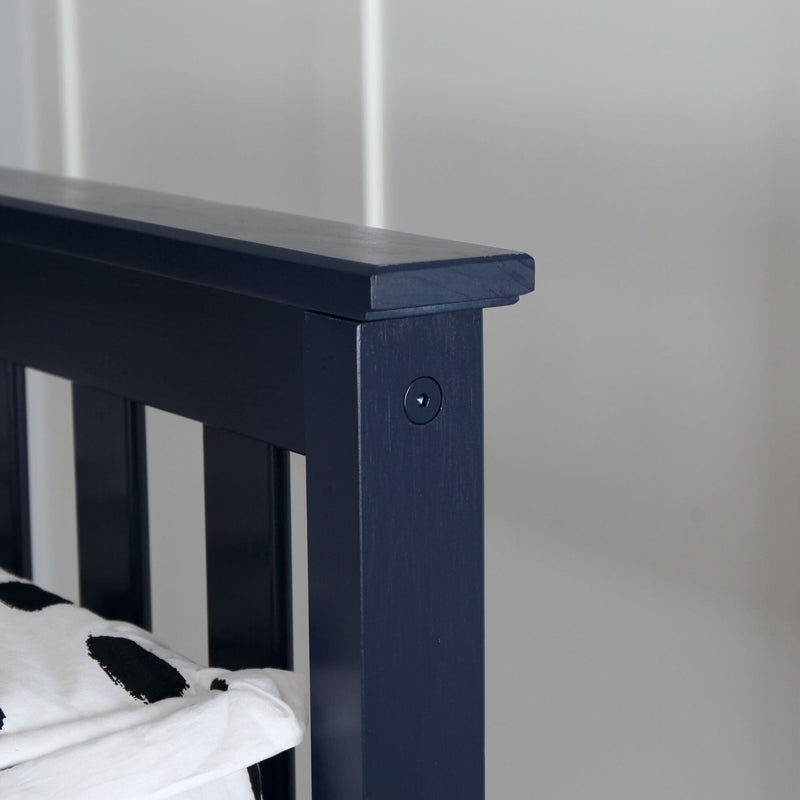 Close-up detail of navy blue painted wooden bed frame headboard post with black and white patterned bedding against a light gray bedroom wall
