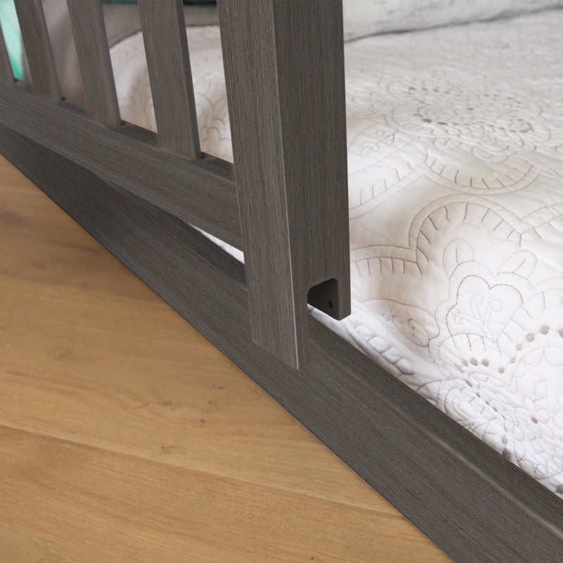 Close-up of modern gray wood bed frame rail on hardwood floor with white quilted mattress