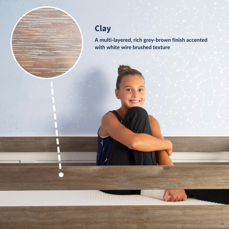Child sitting on a wooden bed showcasing "Clay" multi-layered grey-brown finish with white wire-brushed texture, close-up sample and constellation wallpaper background