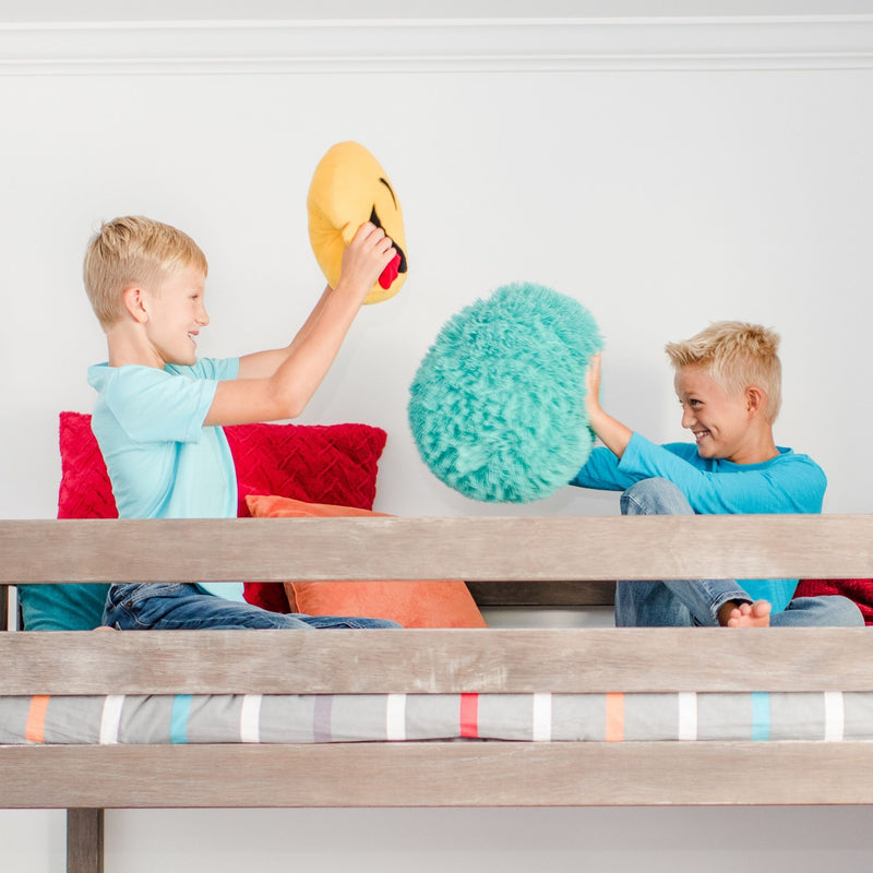 Kids pillow fight on a wooden bunk bed with colorful cushions and a teal fuzzy pillow in a bright kids' bedroom