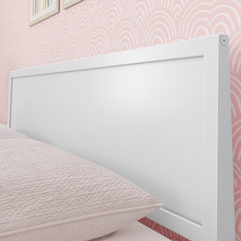 Close-up of white wooden headboard with textured pink bedding and scallop-pattern pink wallpaper in girls' bedroom decor