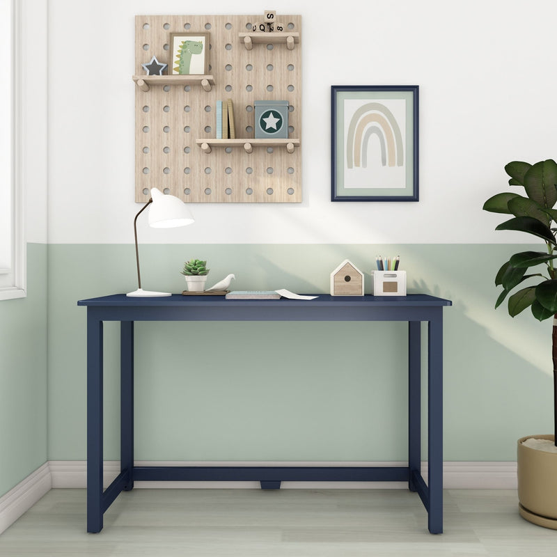 Minimalist kids' study nook with navy desk, wooden pegboard shelves, framed rainbow wall art, white desk lamp and potted plant