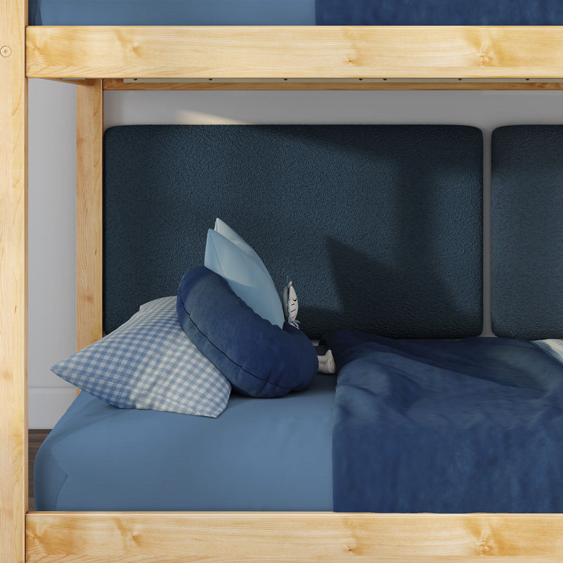 Close-up of lower bunk bed with natural wood frame, layered blue bedding, navy textured cushions and gingham pillow