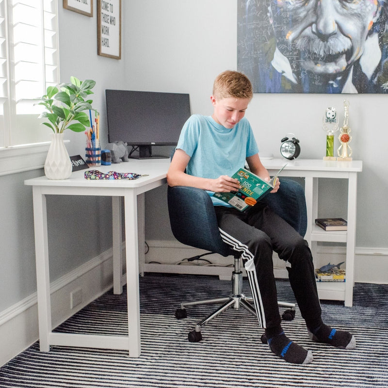 Boy reading a science book in a bright modern home study with white desk, computer monitor, trophies, potted plant and large portrait on the wall