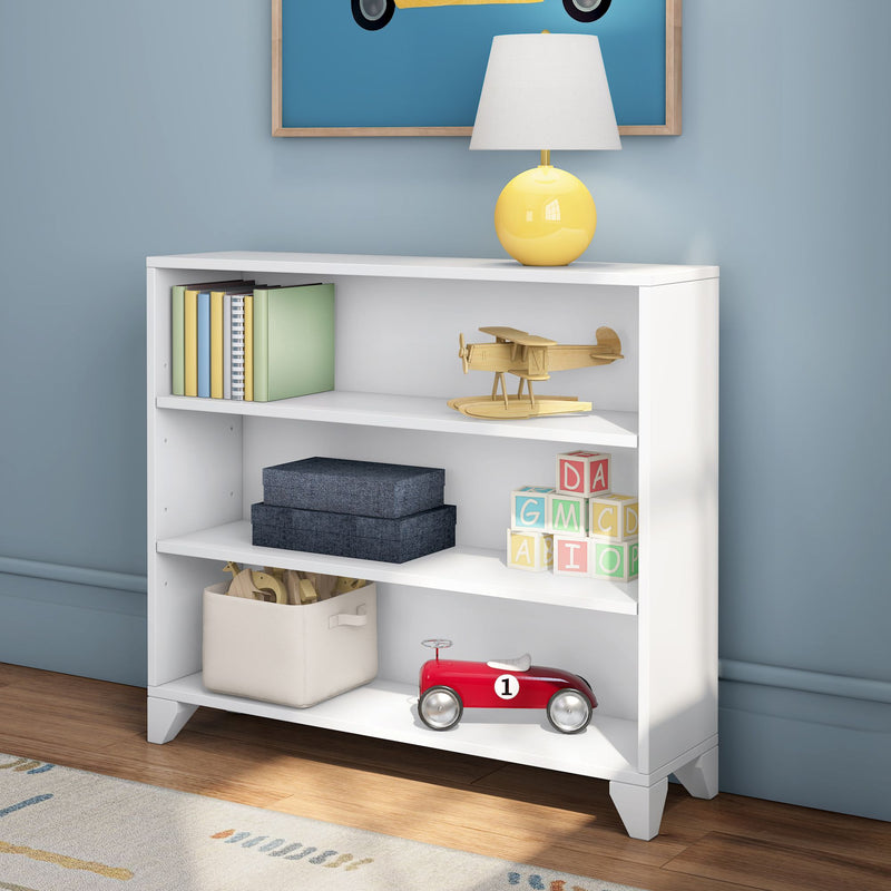 White kids bookshelf in blue nursery with yellow table lamp, wooden toy airplane, colorful board books, alphabet blocks, fabric storage bin and red toy car — children's room storage and nursery decor