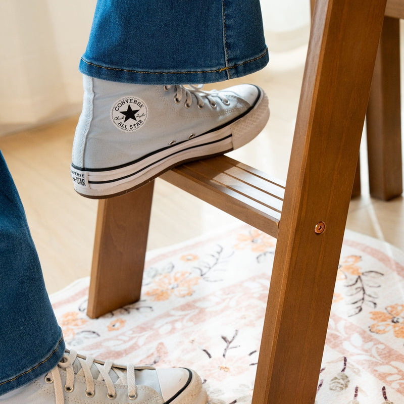 Close-up of white Converse Chuck Taylor All Star high-top sneakers with blue jeans resting on a wooden step stool over a patterned rug