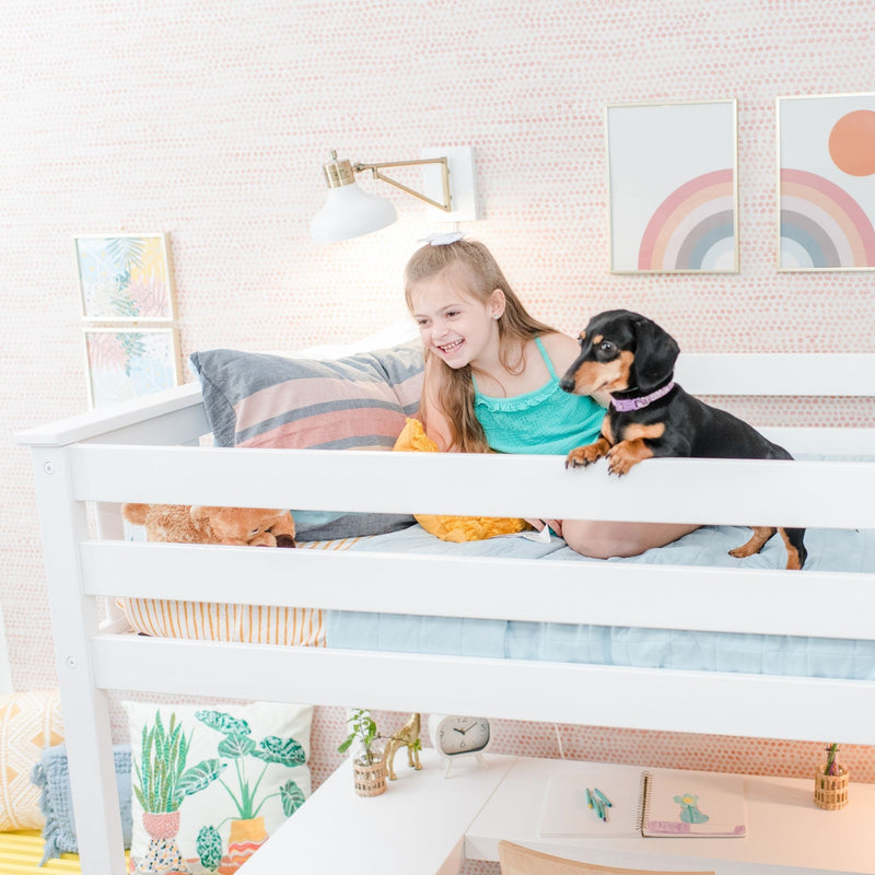 Smiling girl with black dachshund on white bunk bed in pastel kids bedroom with pink dot wallpaper and rainbow wall art