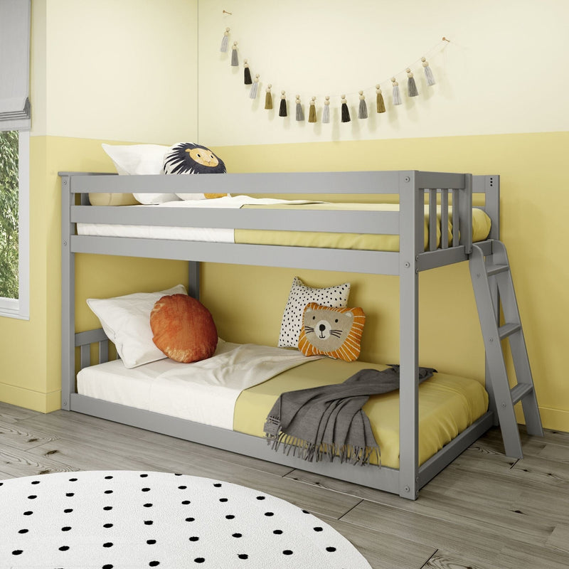 Gray wooden bunk bed in a modern children's bedroom with yellow bedding, decorative tassel garland, lion throw pillow, polka-dot rug and ladder on light wood floor