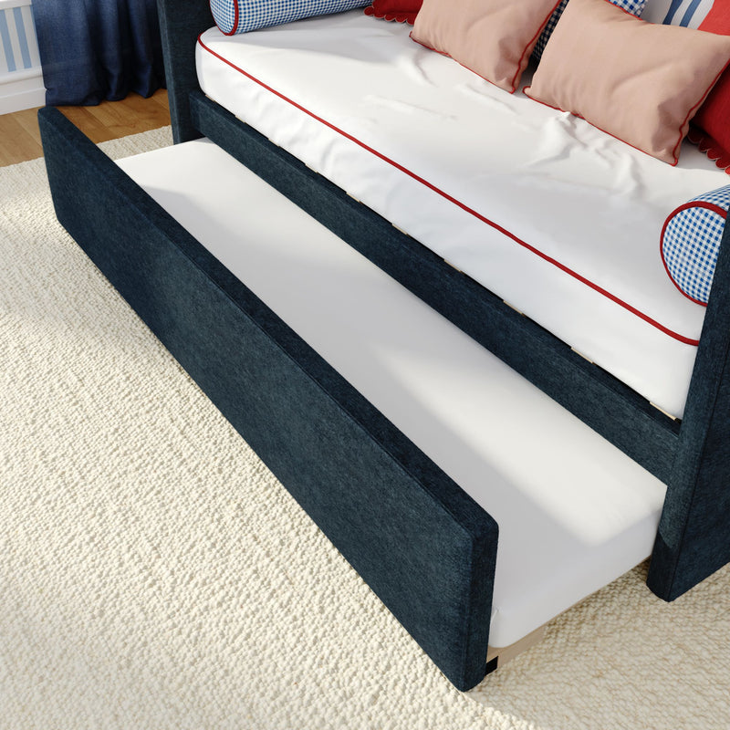Navy upholstered daybed with pull-out trundle, white mattress with red piping and decorative pillows on cream rug.