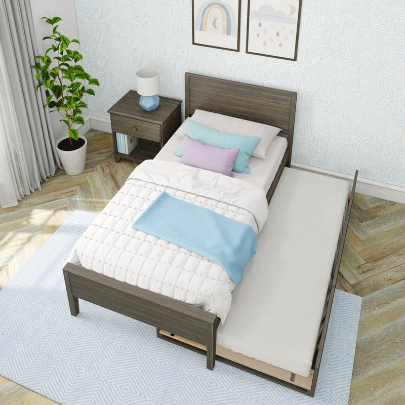 Modern wooden twin bed with pull-out trundle, pastel blue and lavender bedding, wood nightstand with blue geometric lamp, potted plant and patterned wallpaper in bright kids' bedroom