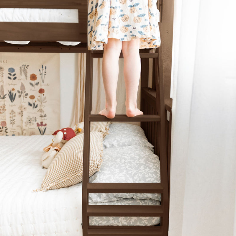 Child's bare feet on a wooden bunk bed ladder in a cozy kids' bedroom with patterned bedding, gingham pillows and botanical wall art