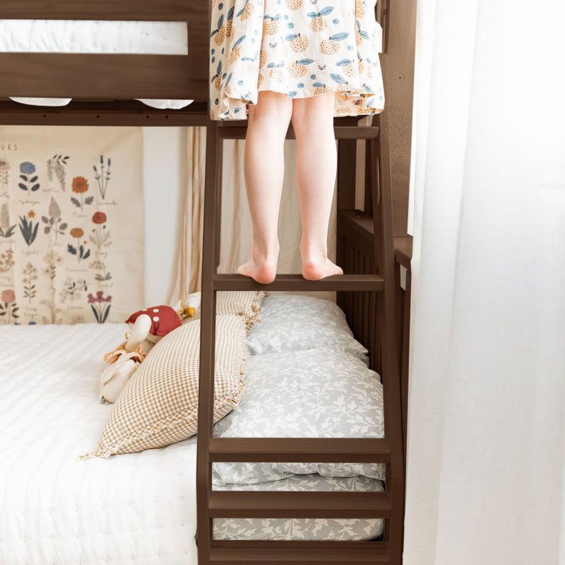 Child's bare feet on a wooden bunk bed ladder in a cozy kids' bedroom with patterned bedding, gingham pillows and botanical wall art