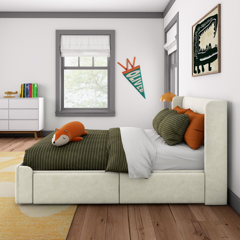 Modern children's bedroom with green striped bedding, orange pillows and fox plush on bed, white upholstered frame, window with Roman shade, Oliver pennant, dinosaur wall art, and white dresser with books and wooden toy plane