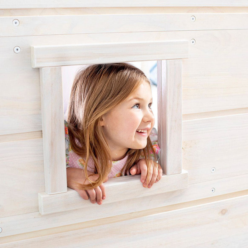Smiling girl peeking through a wooden playhouse window in a bright children's playroom