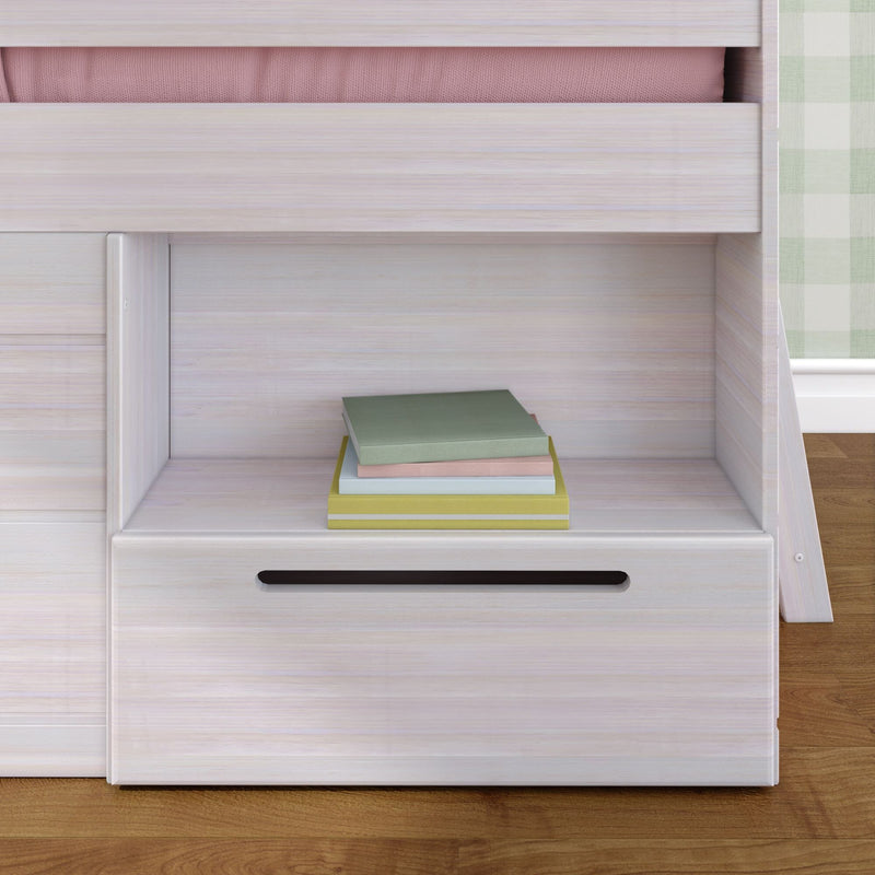 Whitewashed wood bunk bed storage shelf and drawer with stacked pastel books, pink mattress edge, and green plaid curtain in a children’s bedroom