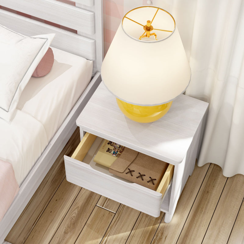 White nightstand with open drawer holding books and burlap pouch, yellow table lamp on top beside bed on wooden floor, modern cozy bedroom decor