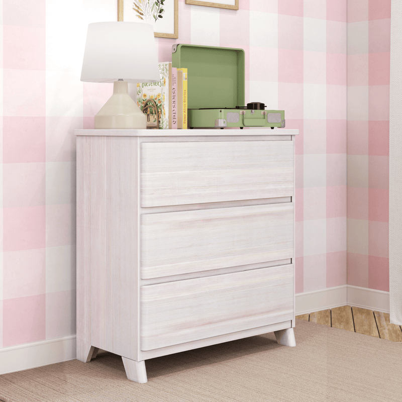 Whitewashed dresser in pink gingham nursery with beige table lamp, green suitcase record player, children's books and framed botanical wall art