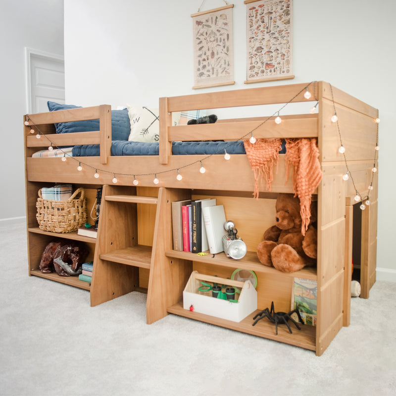 Wooden loft bunk bed with built-in storage shelves and ladder, navy cushions, decorative string lights, wicker baskets and plush toys in a bright kids' bedroom