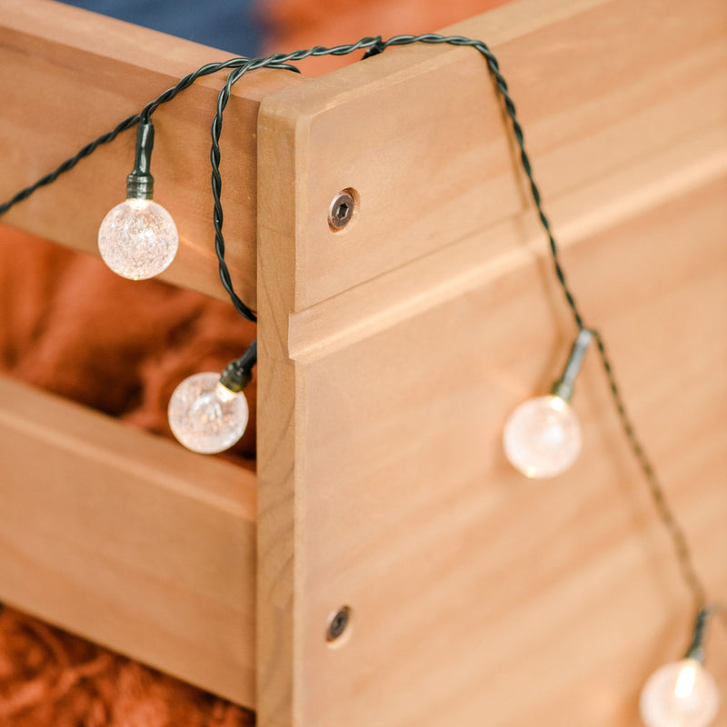 Crackle globe string lights draped over a wooden bed frame providing cozy bedroom ambient lighting and rustic home decor