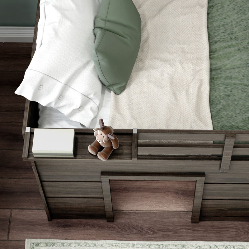 Top-down view of a modern wooden baby crib with white pillow, sage-green accent pillow, beige textured blanket and plush moose toy, nursery bedding and decor