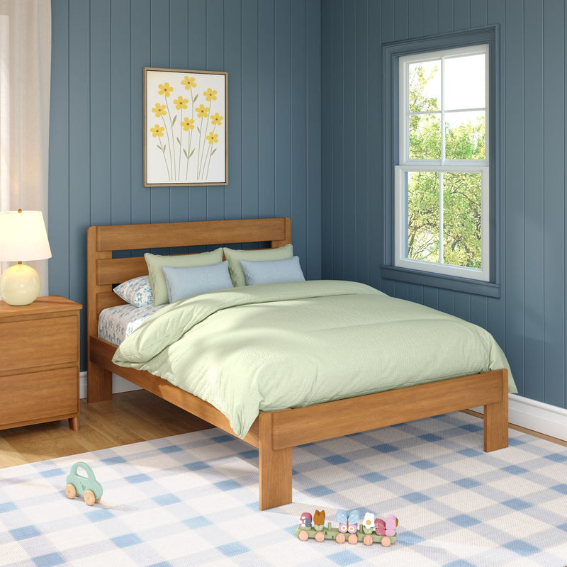Cozy children's bedroom interior with blue vertical paneled walls, wooden bed and green bedding, yellow flower wall art, nightstand lamp, window with tree view and wooden toy train on a blue checkered rug