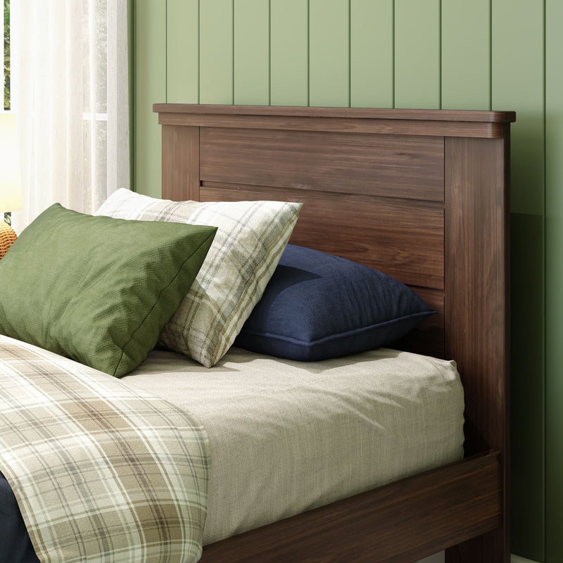 Walnut wood headboard with green pillows, plaid blanket and navy pillow against sage-green paneled wall with sheer curtains in cozy bedroom