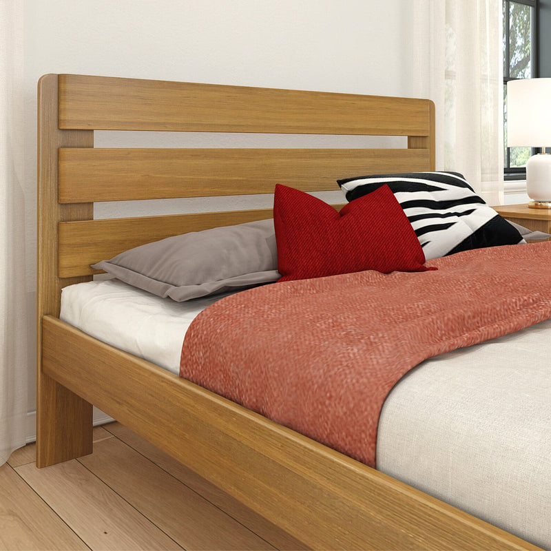 Modern natural wood platform bed with slatted headboard, red accent pillows, striped cushion, beige bedding and bedside lamp