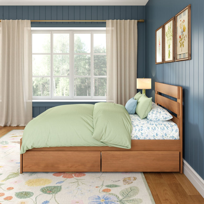 Cozy bedroom with wooden platform bed, light green bedding and floral sheets, floral area rug, blue vertical-paneled accent wall with framed botanical prints, large window with sheer curtains and brass curtain rod
