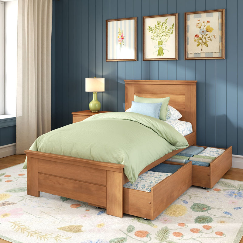Wooden twin storage bed with green bedding and pull-out underbed drawers against a blue paneled wall with floral framed art, nightstand lamp and beige curtains
