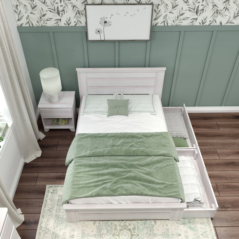 Overhead view of a cozy modern farmhouse bedroom featuring a whitewashed wooden twin bed with green duvet and pillows, sage green board-and-batten accent wall topped with botanical wallpaper, bedside table with lamp, trundle drawer and dark hardwood flooring.