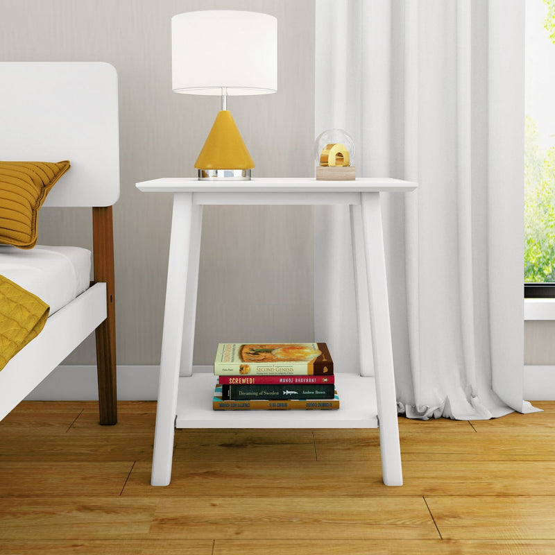 Modern bedroom nightstand with white bedside table, yellow cone table lamp, stacked books on shelf, mustard pillow and white curtains on hardwood floor
